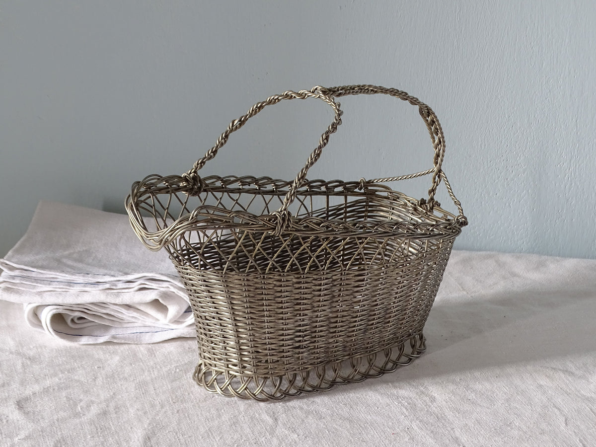 French vintage woven metal bottle basket on a country table with antique linen