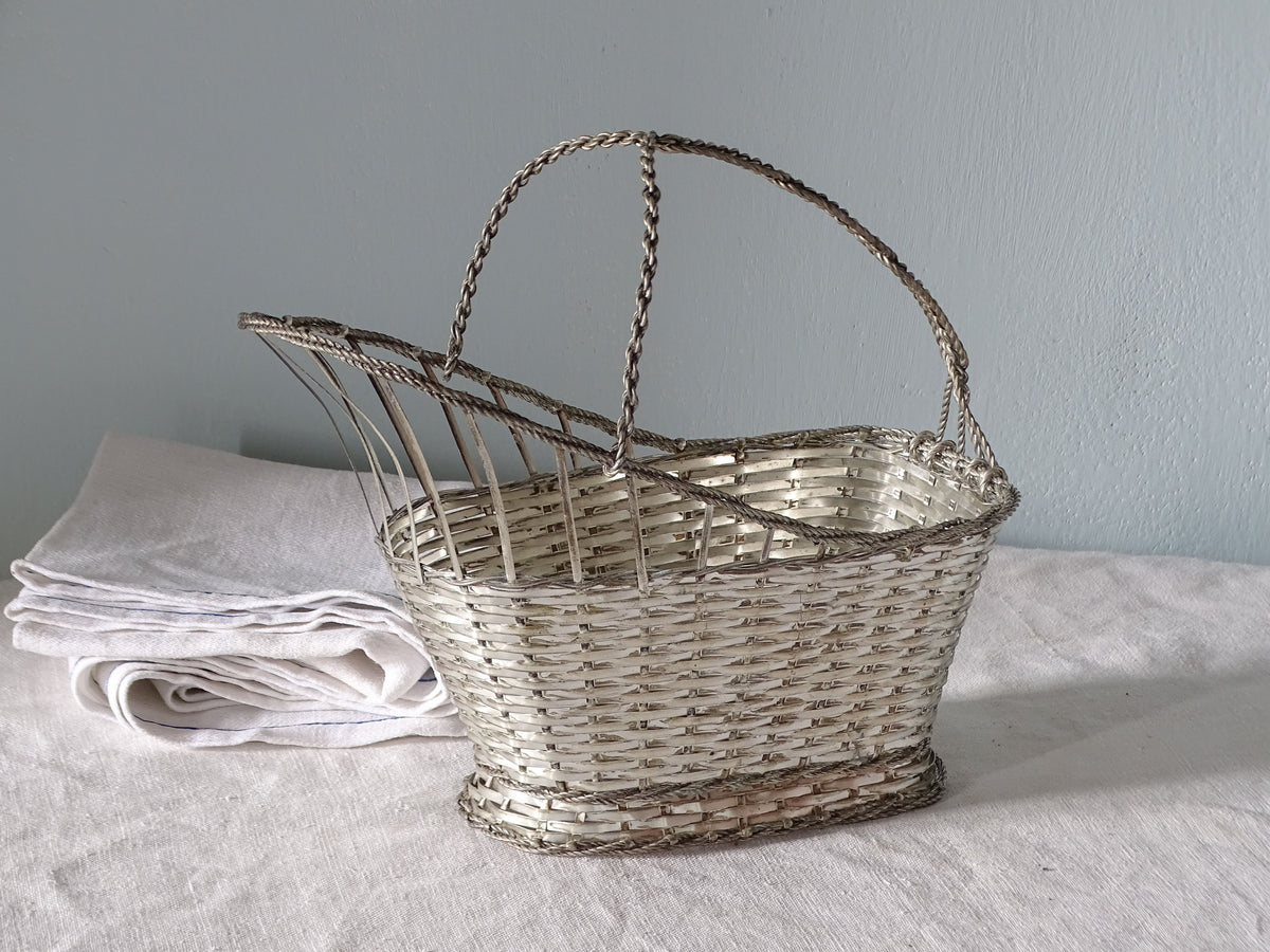 French vintage woven metal bottle carrier with twisted wire handle, displayed on a country house table with antique linen
