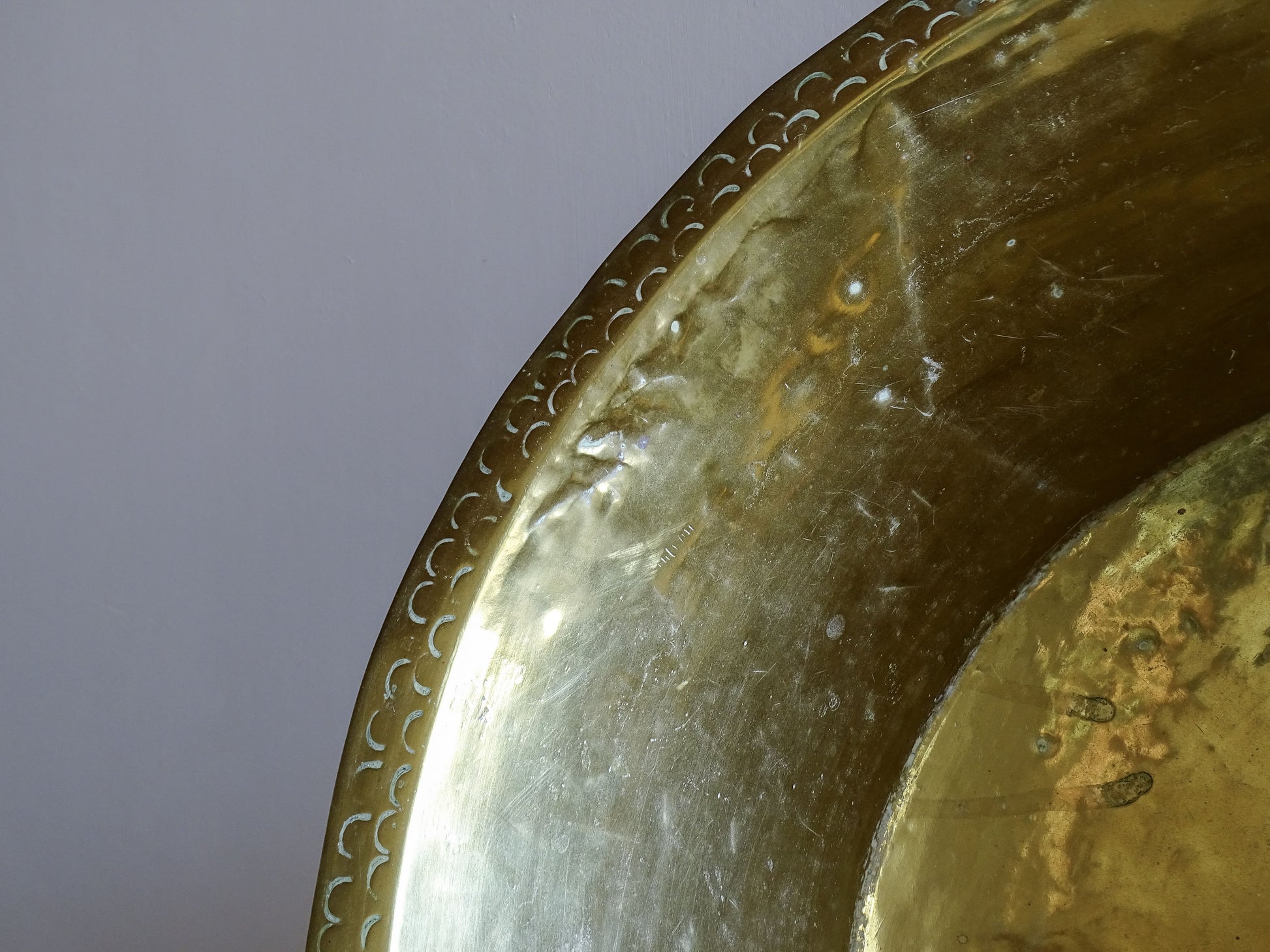 Close-up of the punched crescent decoration and hand-hammered surface of a large antique brass basin.