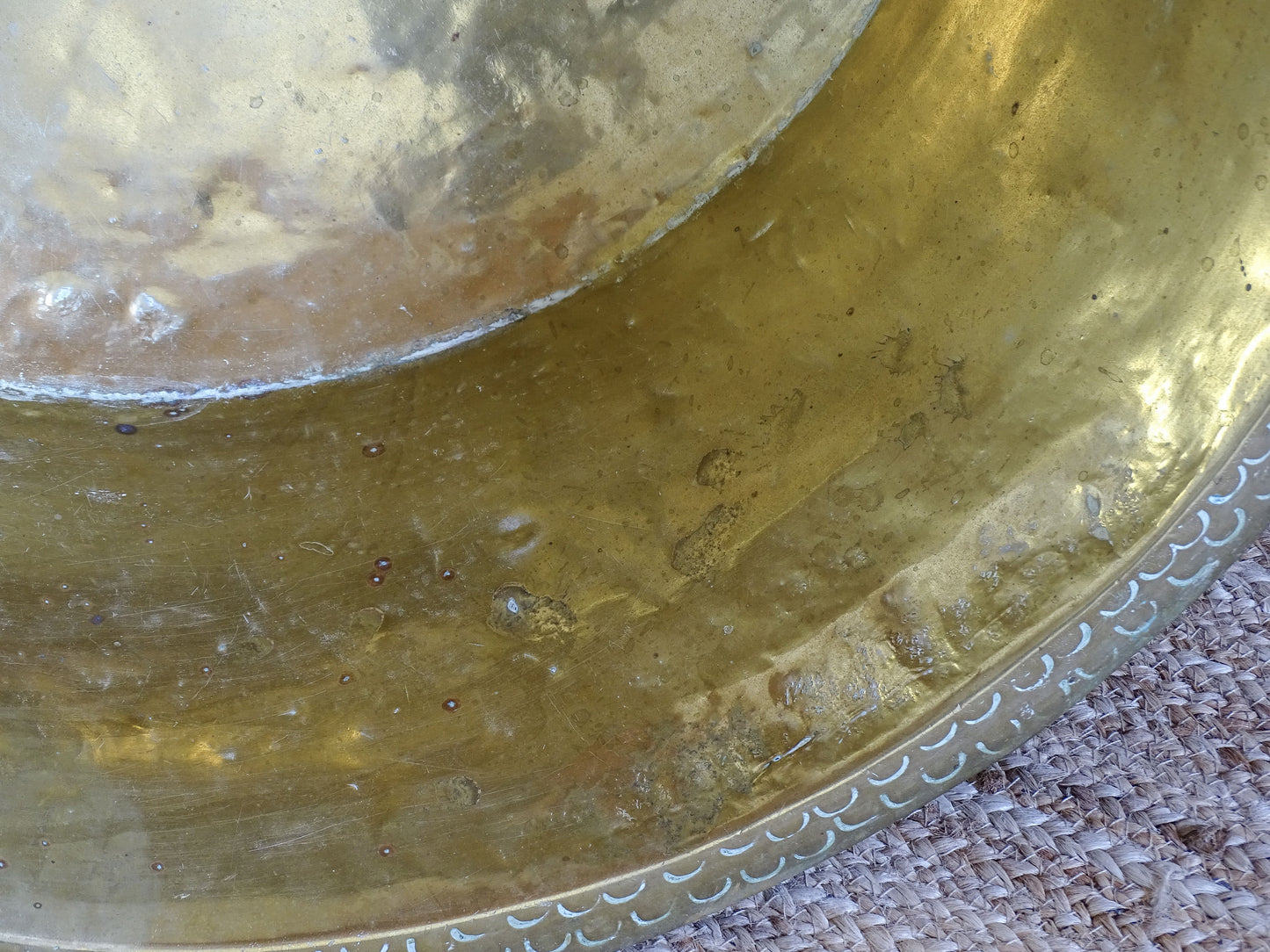 Interior detail of an antique hammered brass basin showing aged marks, oxidation and an old soldered base seam.