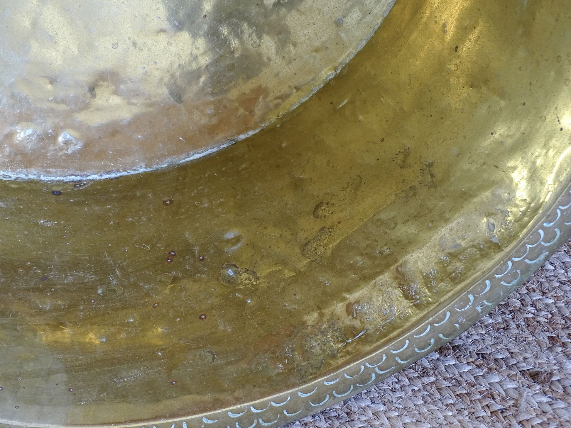 Interior detail of an antique hammered brass basin showing aged marks, oxidation and an old soldered base seam.