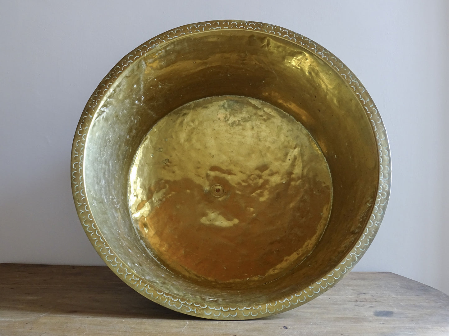 Front view of a 69 cm antique hammered brass basin with a broad rim and repeated punched crescent decoration.