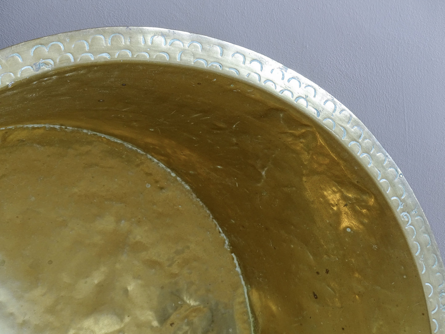 Detailed view of the double row of crescent motifs around the rim of a hand-worked antique brass basin.