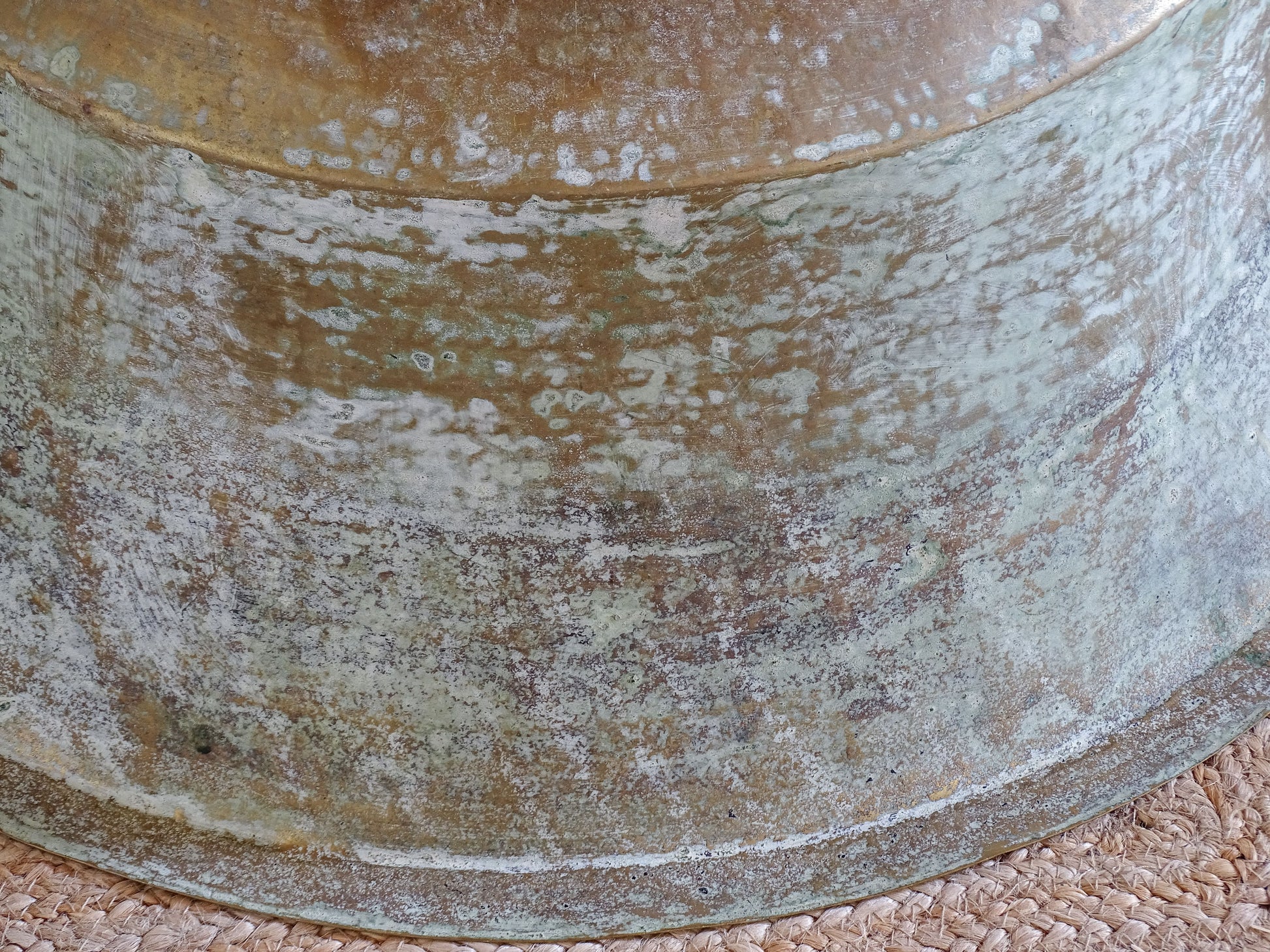 Close-up of the naturally aged green, blue and brown patina covering the exterior of an antique brass basin.