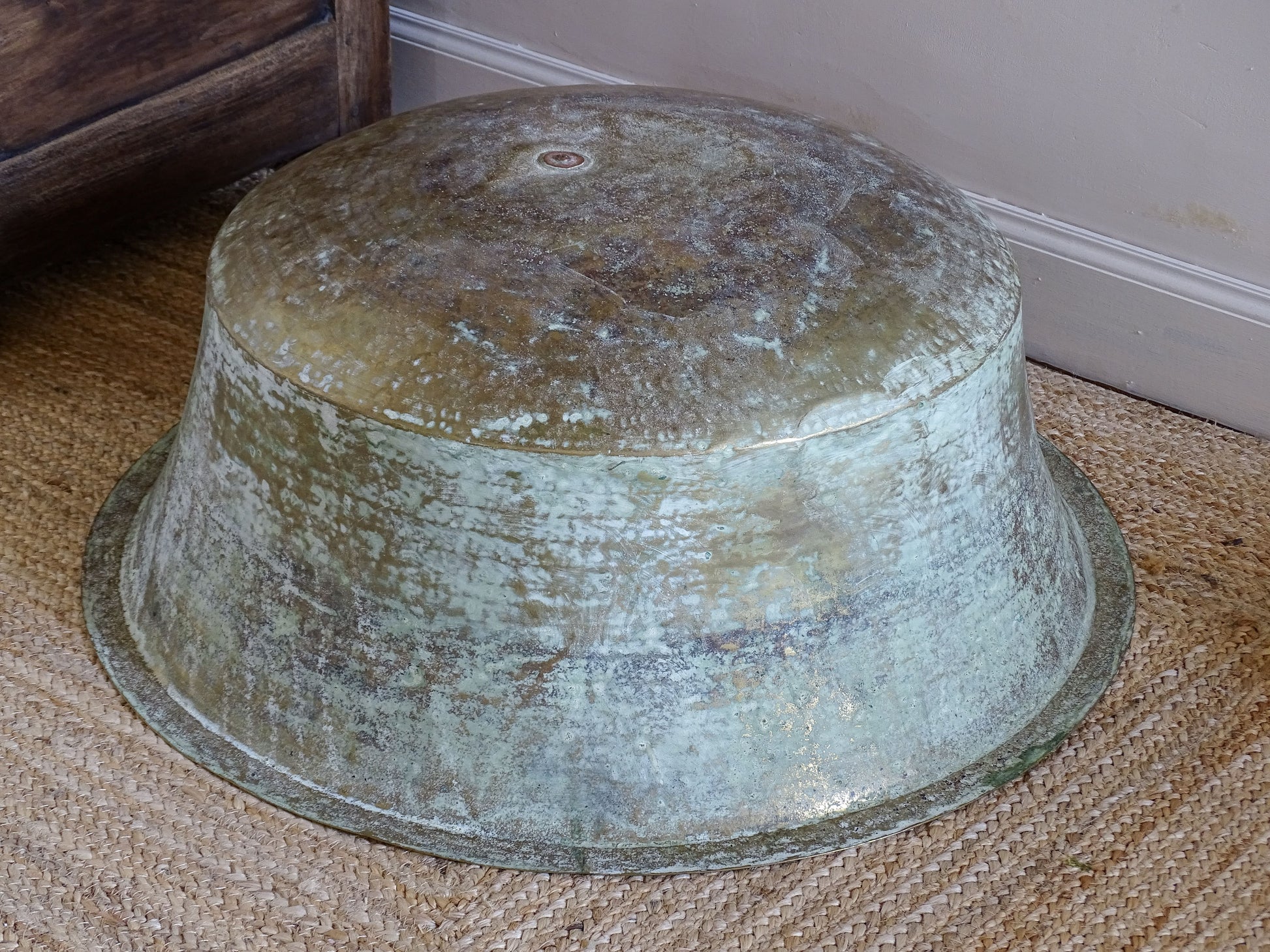 Underside of a large antique brass basin showing extensive natural oxidation, hammer marks and an old central plug.