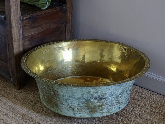 Side view of a large antique brass basin with a golden interior, flared rim and heavily patinated exterior.