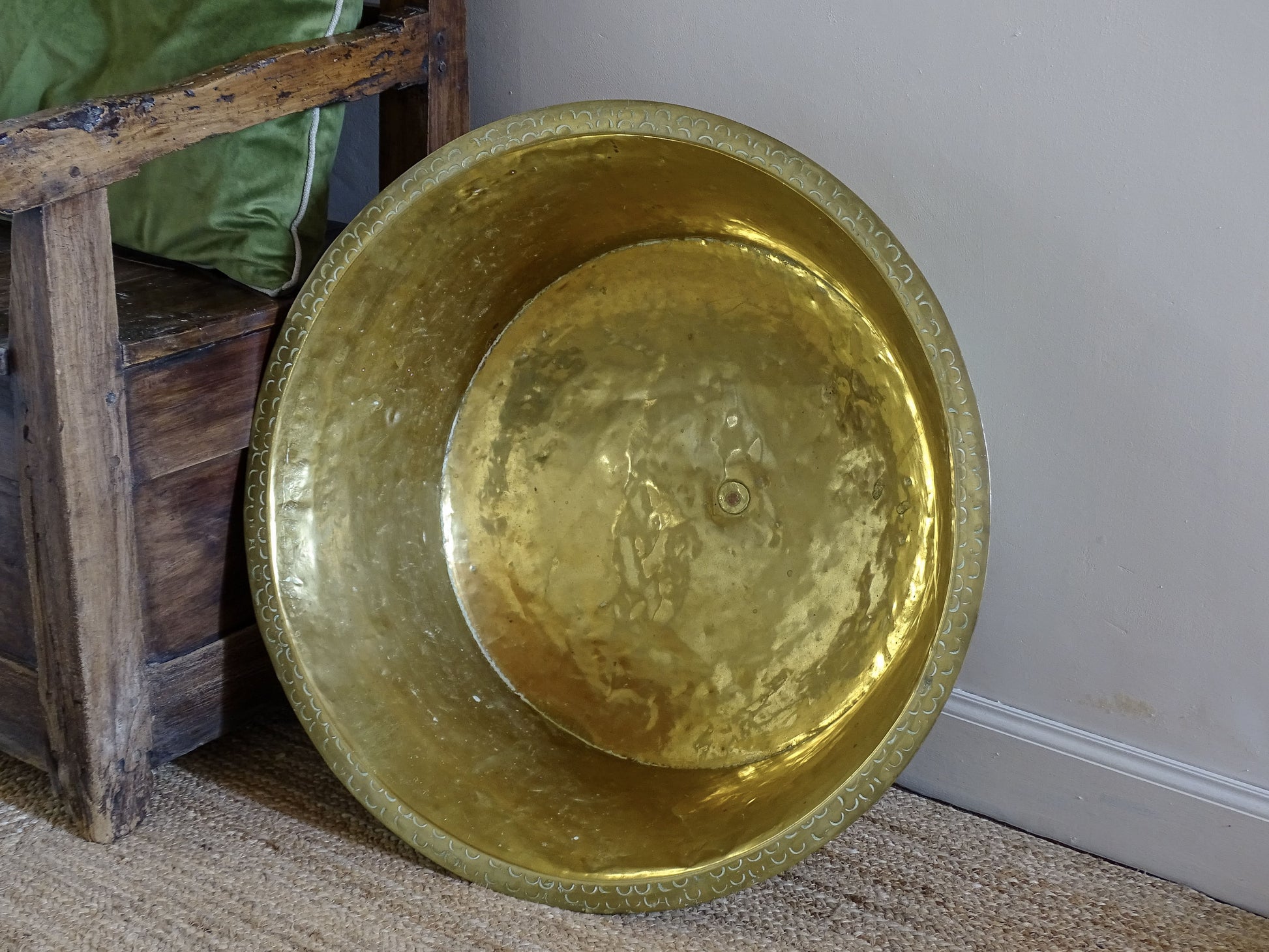 Large hand-hammered antique brass basin displayed upright beside a rustic wooden chair.