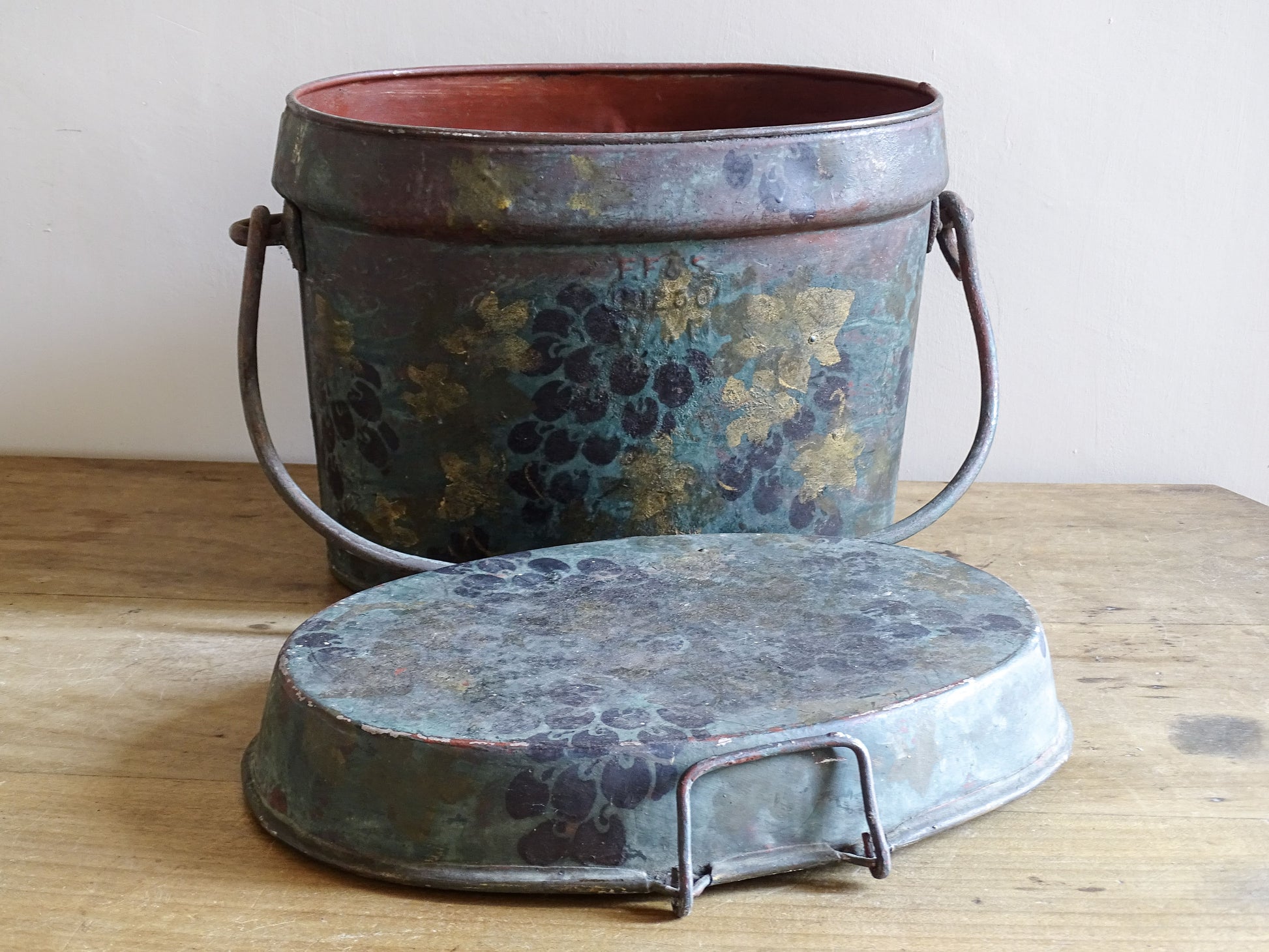 Vintage oval metal box with painted grape decoration and its fitted lid resting in the foreground.