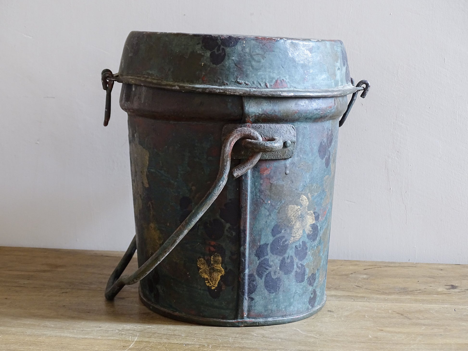 Side view of the vintage painted metal box with its broad carrying handle lowered across the body.