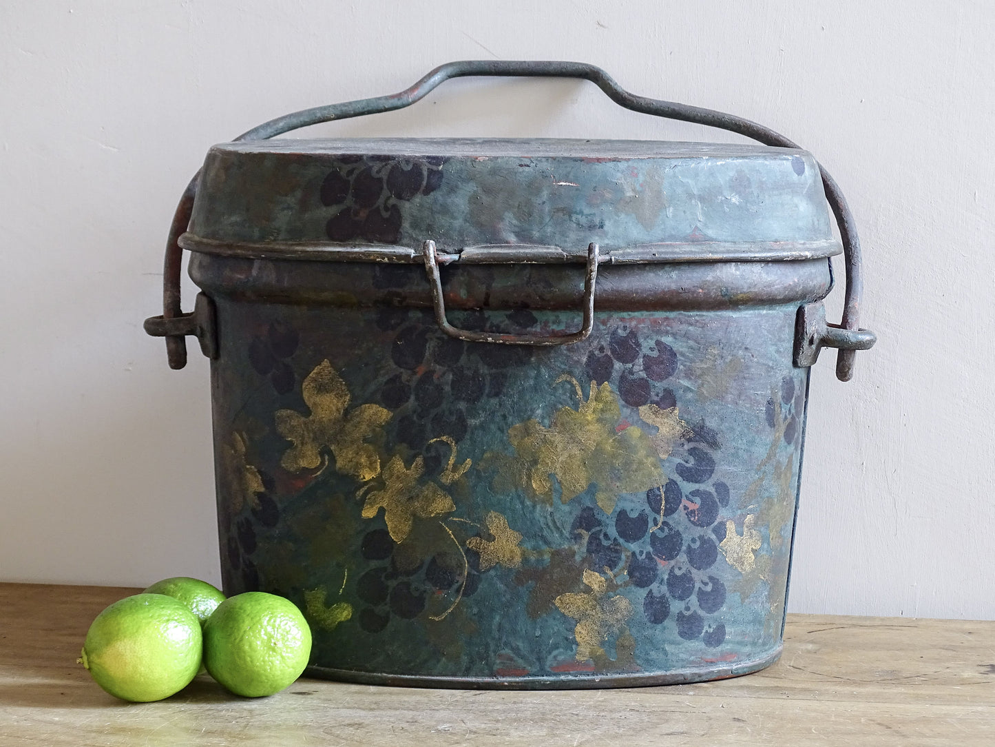 Large grape-painted toleware storage box displayed with green limes to show its generous proportions.