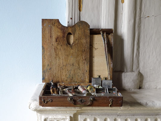 French antique art box with palette and paint contents, pictured on a country house fireplace
