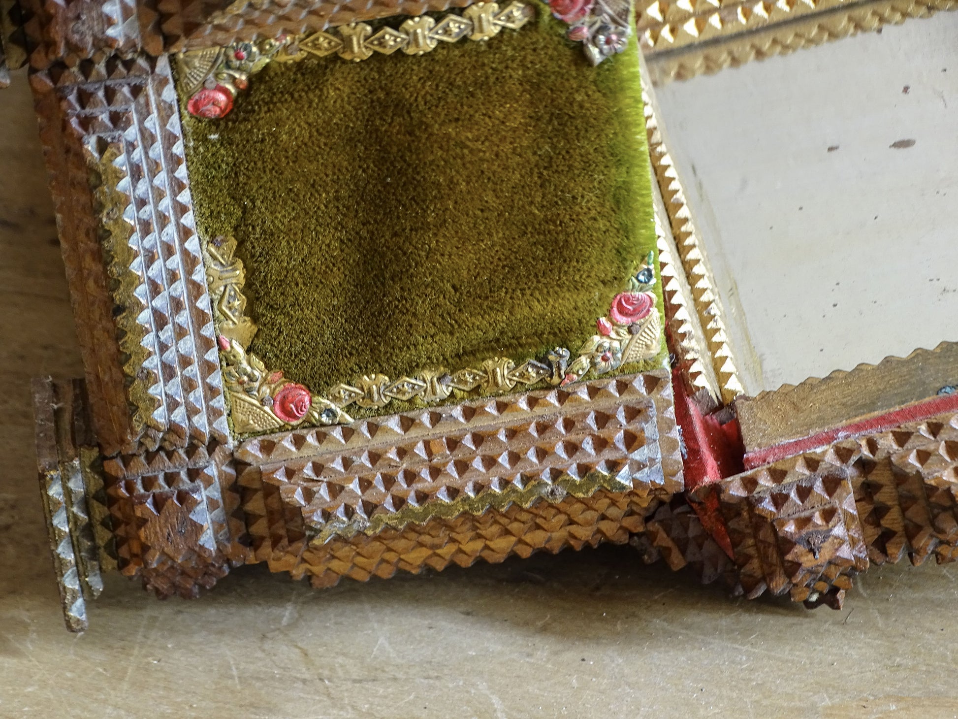 Close-up of olive green velvet side panel on antique tramp art box with gilt floral trim, painted roses and layered chip-carved wood.