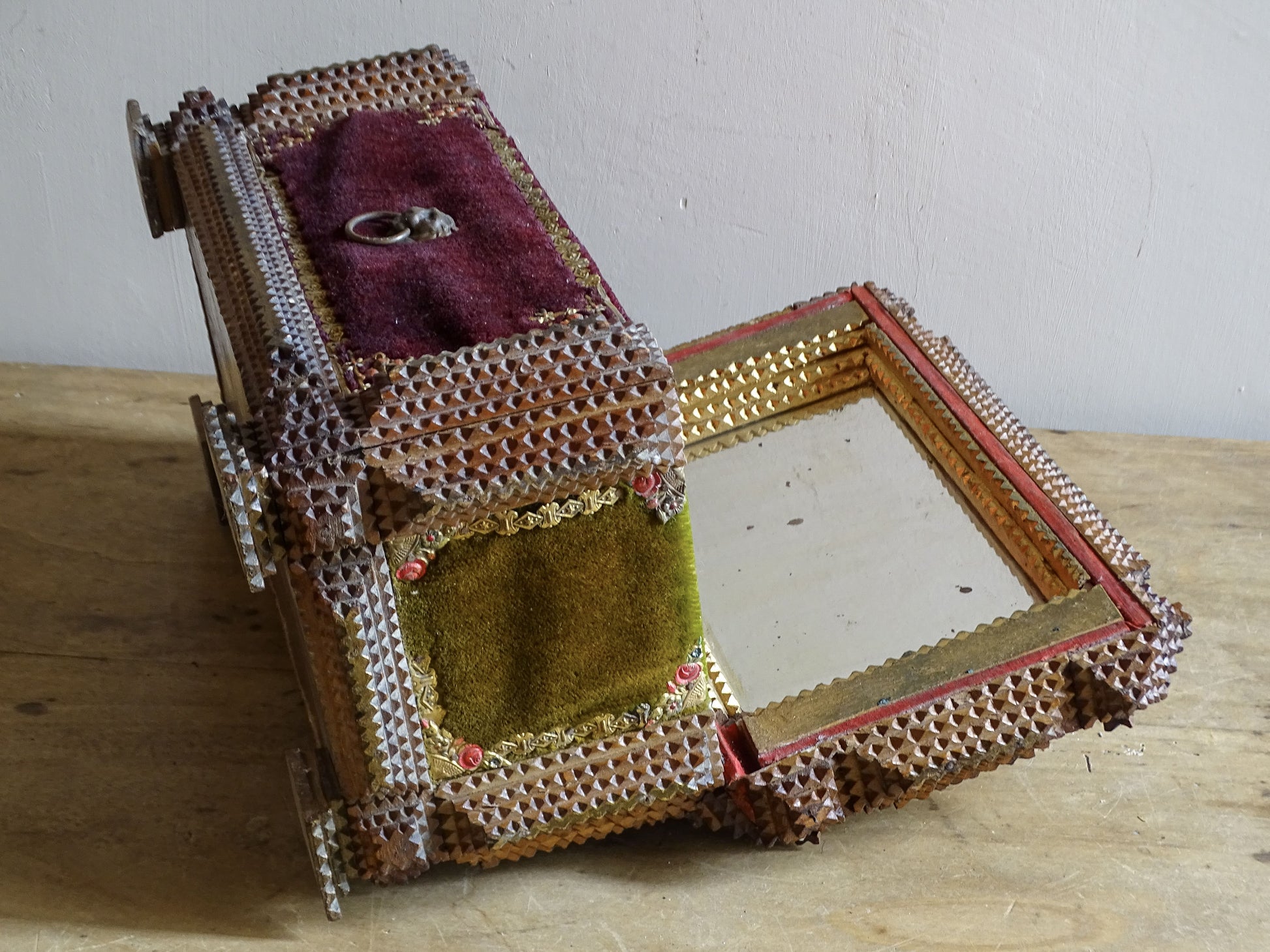 Open antique tramp art box with its mirrored lid, olive velvet side panel and architectural carved woodwork.