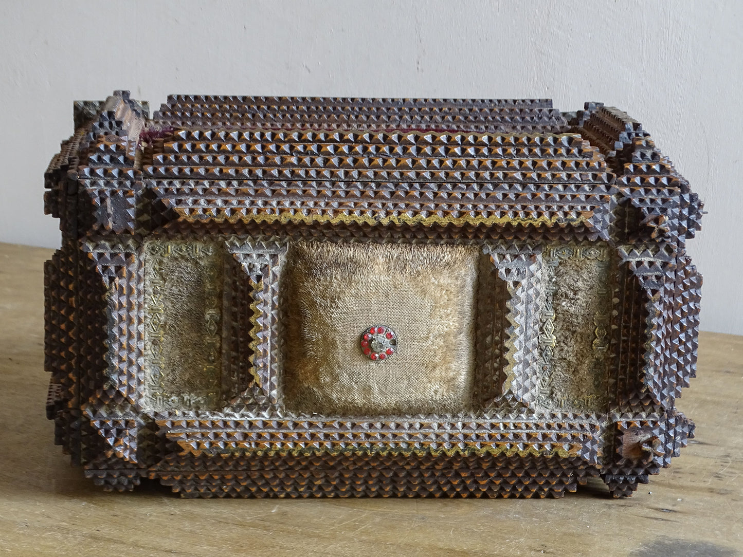 Reverse of antique tramp art box with faded cream fabric panels, central red glass detail and elaborate layered chip carving.