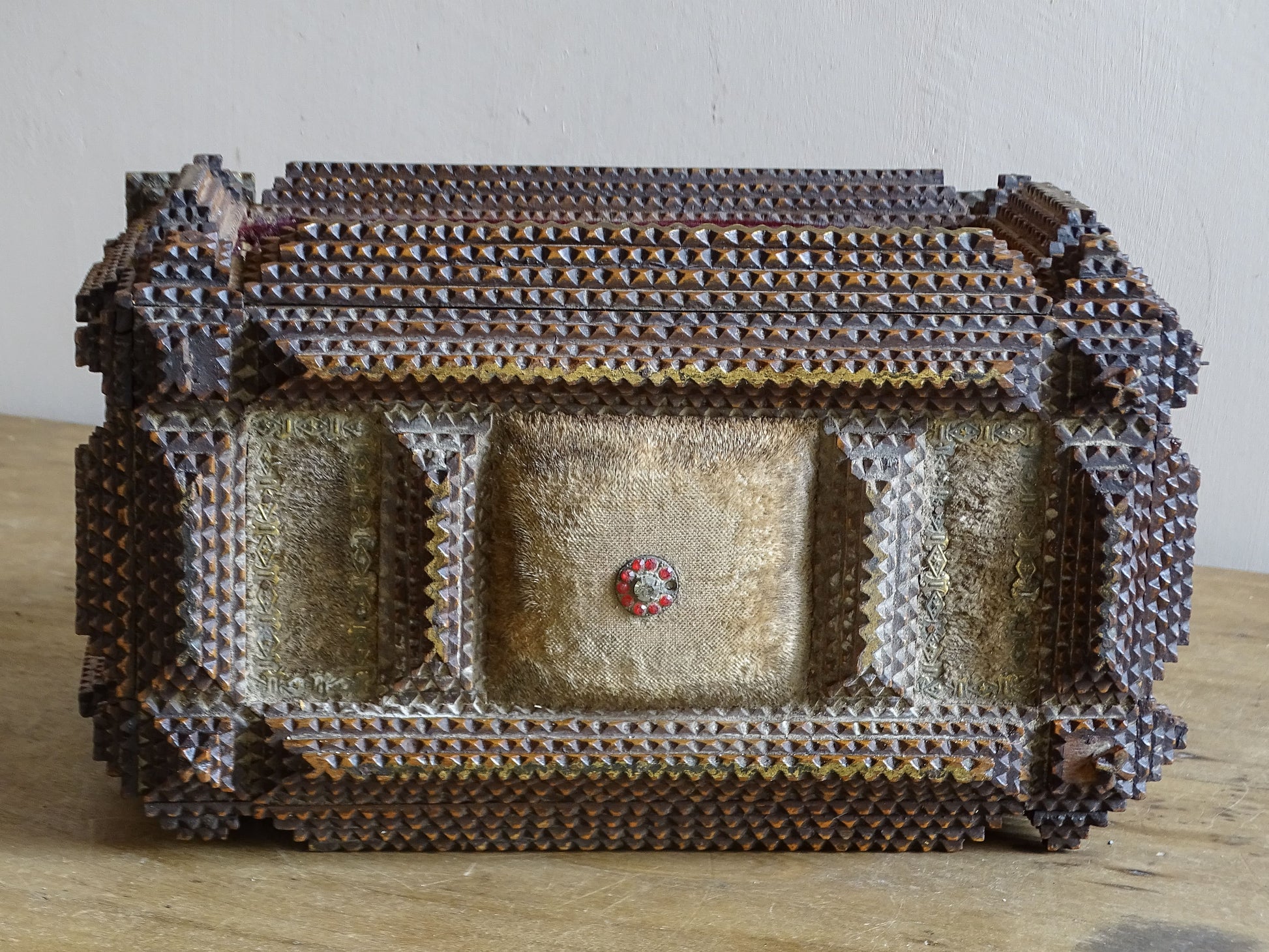 Reverse of antique tramp art box with faded cream fabric panels, central red glass detail and elaborate layered chip carving.