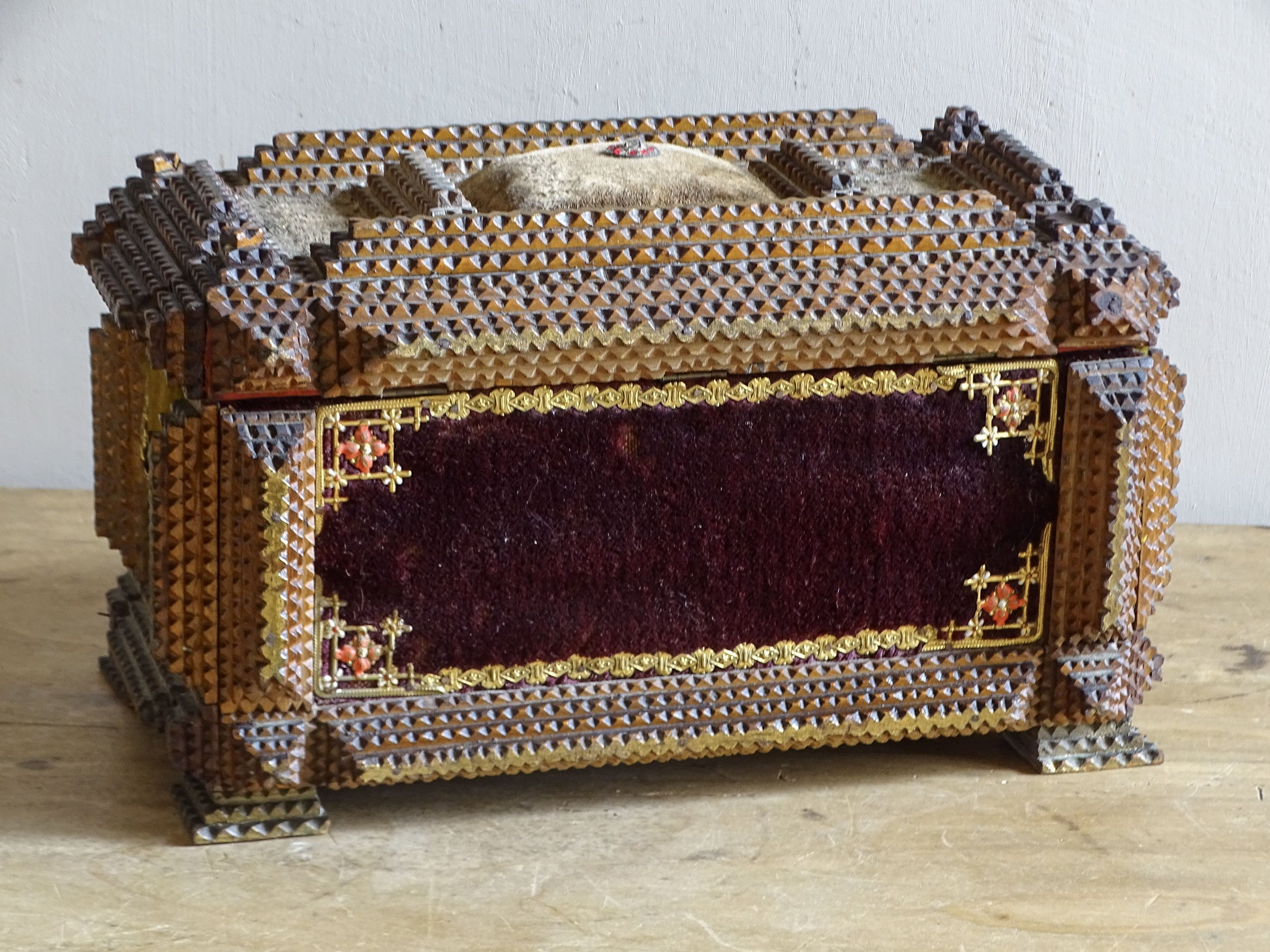 Burgundy velvet panel on antique tramp art box with gilt floral corner mounts and raised pincushion visible above.