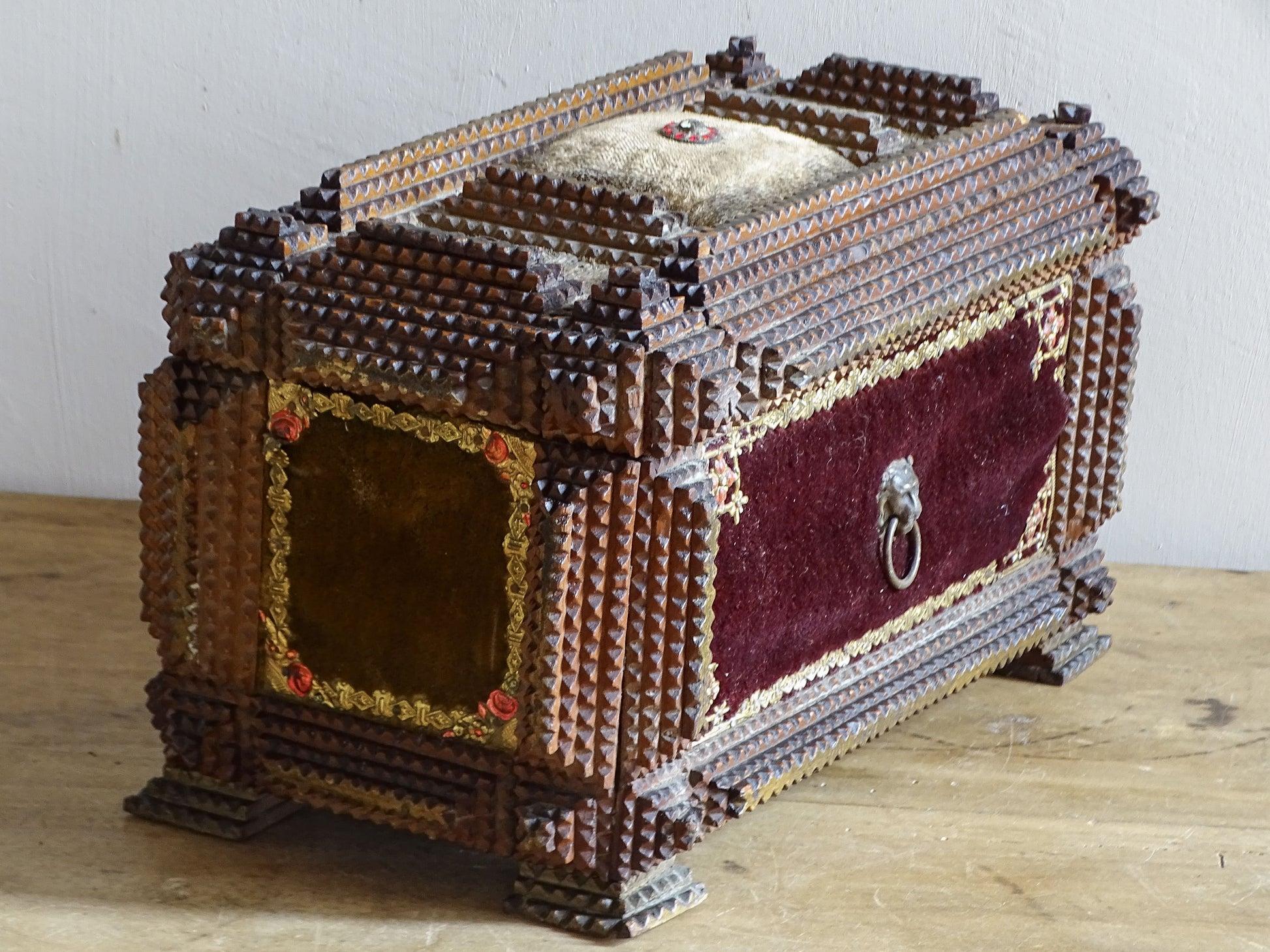 Angled view of antique tramp art box displaying its layered chip carving, velvet panels and gilt rose decoration.