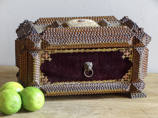 Front view of ornate antique tramp art box with burgundy velvet panel, lion-mask ring handle and raised fabric pincushion.