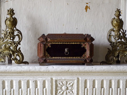 Ornate antique tramp art box with burgundy velvet panel, lion-mask ring handle and raised fabric pincushion on a fireplace. 