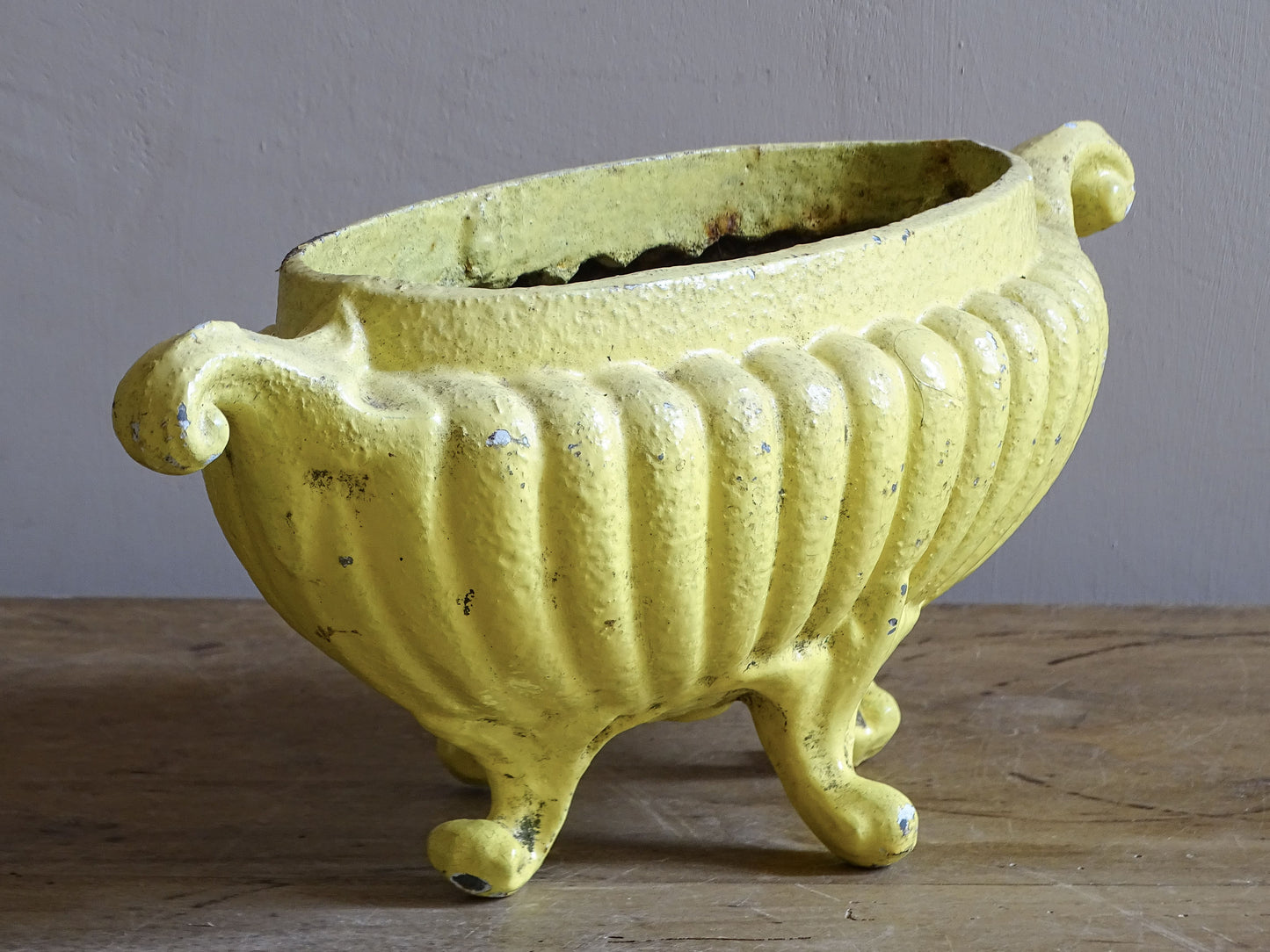 Small antique French cast iron planter with aged yellow paint, decorative handles and raised feet.