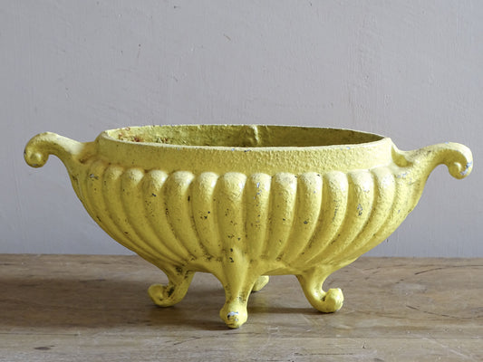 Yellow antique French cast iron planter with ribbed sides, scroll feet and aged patina.