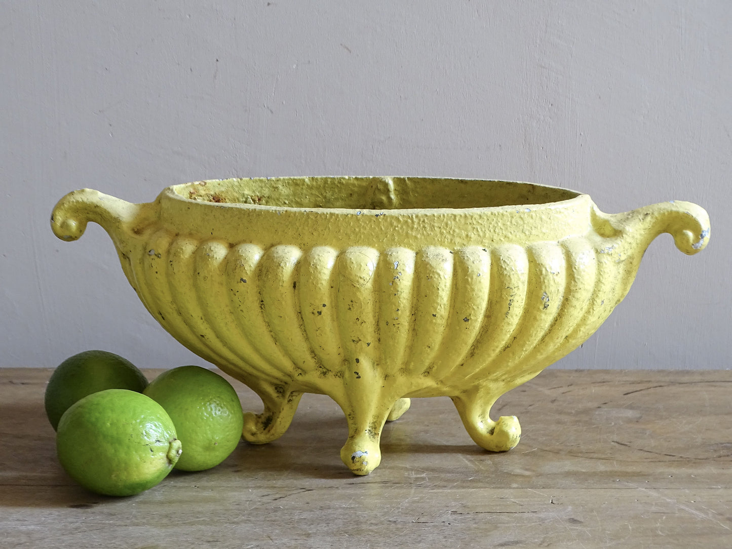 Antique French cast iron jardinière planter with worn yellow painted finish and scrolling handles.