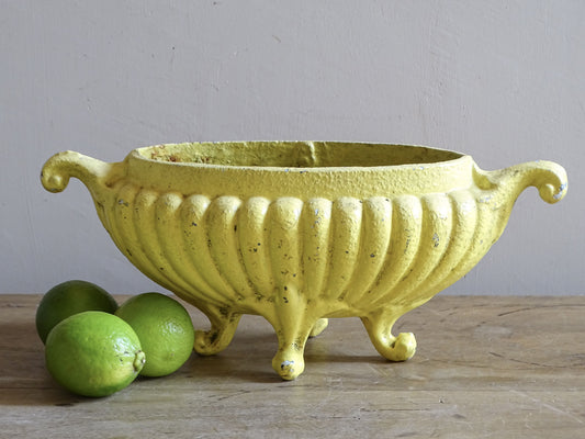 Antique French cast iron jardinière planter with worn yellow painted finish and scrolling handles.