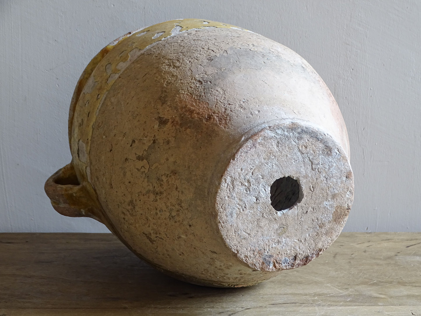 Antique French confit pot lying on its side showing the unglazed earthenware base and later drainage hole.
