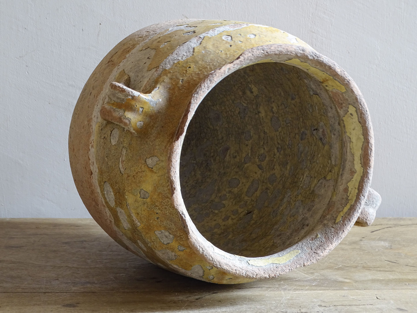 Antique French yellow-glazed confit pot lying on its side, showing the heavily crazed glazed interior and worn rim.
