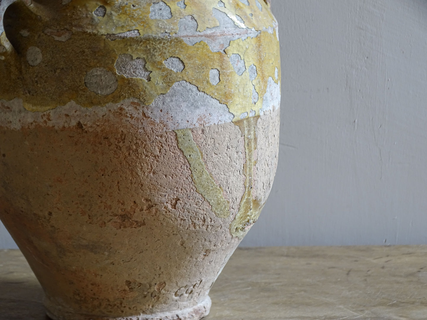 Close-up of a 19th-century French confit pot showing weathered yellow glaze, glaze loss and textured earthenware.