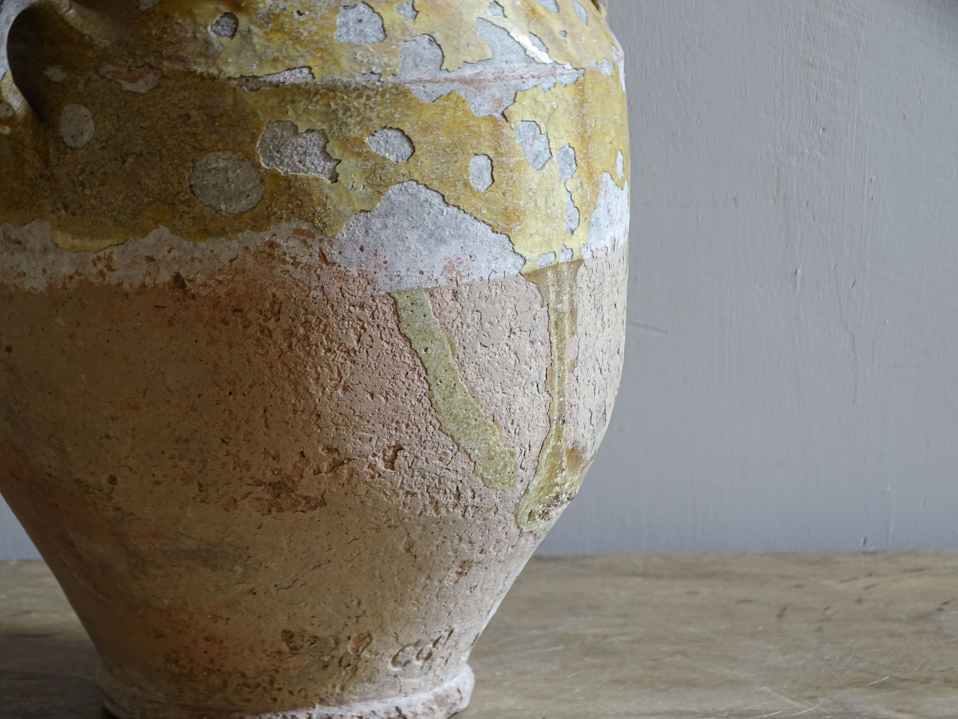 Close-up of a 19th-century French confit pot showing weathered yellow glaze, glaze loss and textured earthenware.