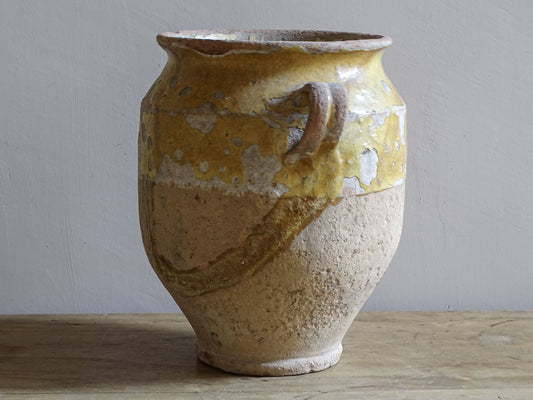 Close-up of a 19th-century French confit pot showing weathered yellow glaze, glaze loss and textured earthenware.