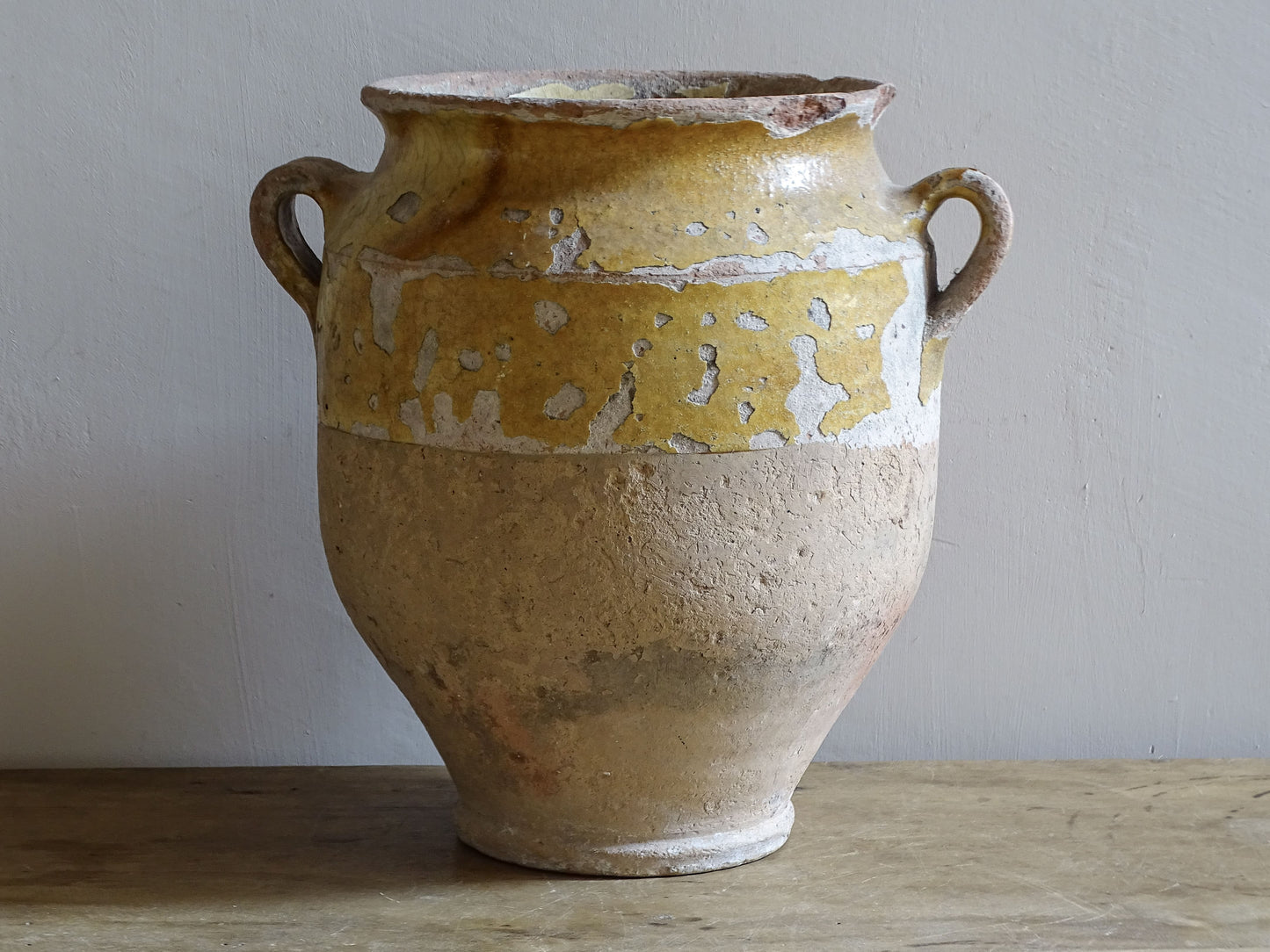 Antique French confit jar with twin handles, worn yellow glaze and decorative glaze runs over the unglazed earthenware body.