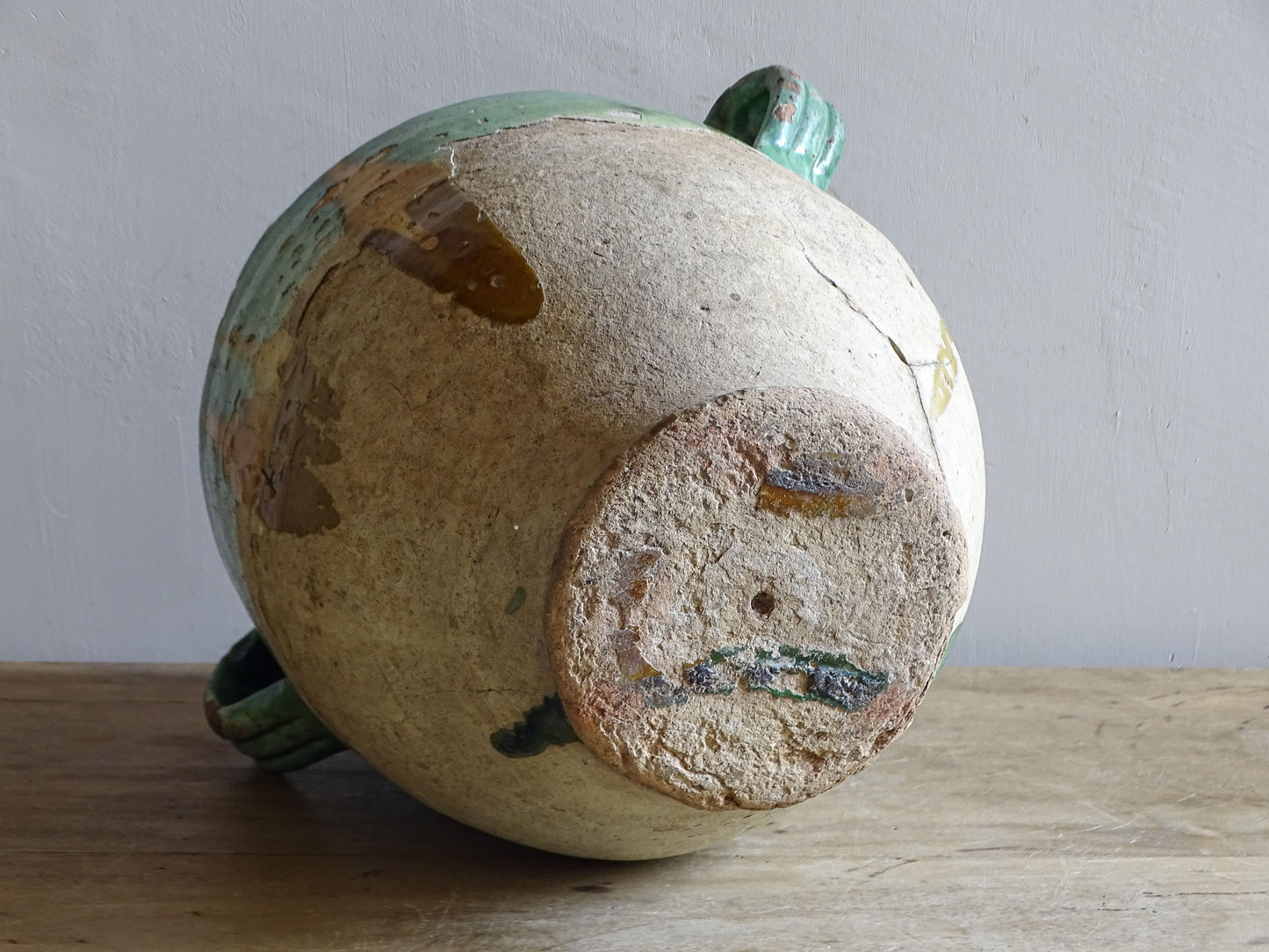 Antique French confit pot with unusual turquoise-green and mustard-yellow glaze, twin handles and a heavily weathered earthenware surface.