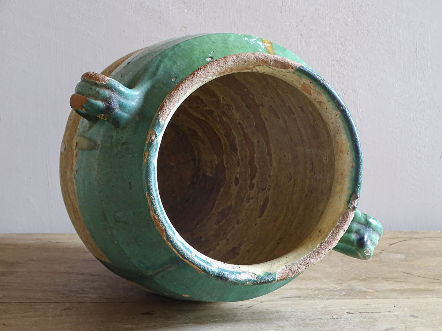 Antique French confit pot with unusual turquoise-green and mustard-yellow glaze, twin handles and a heavily weathered earthenware surface.