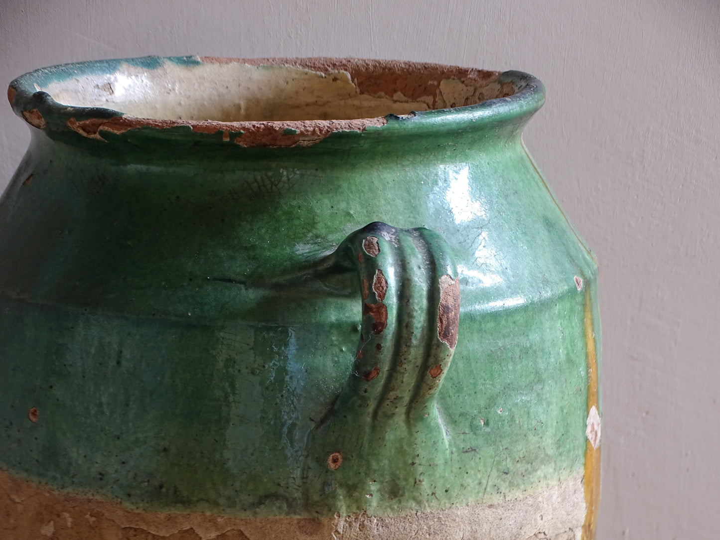 Antique French confit pot with unusual turquoise-green and mustard-yellow glaze, twin handles and a heavily weathered earthenware surface.