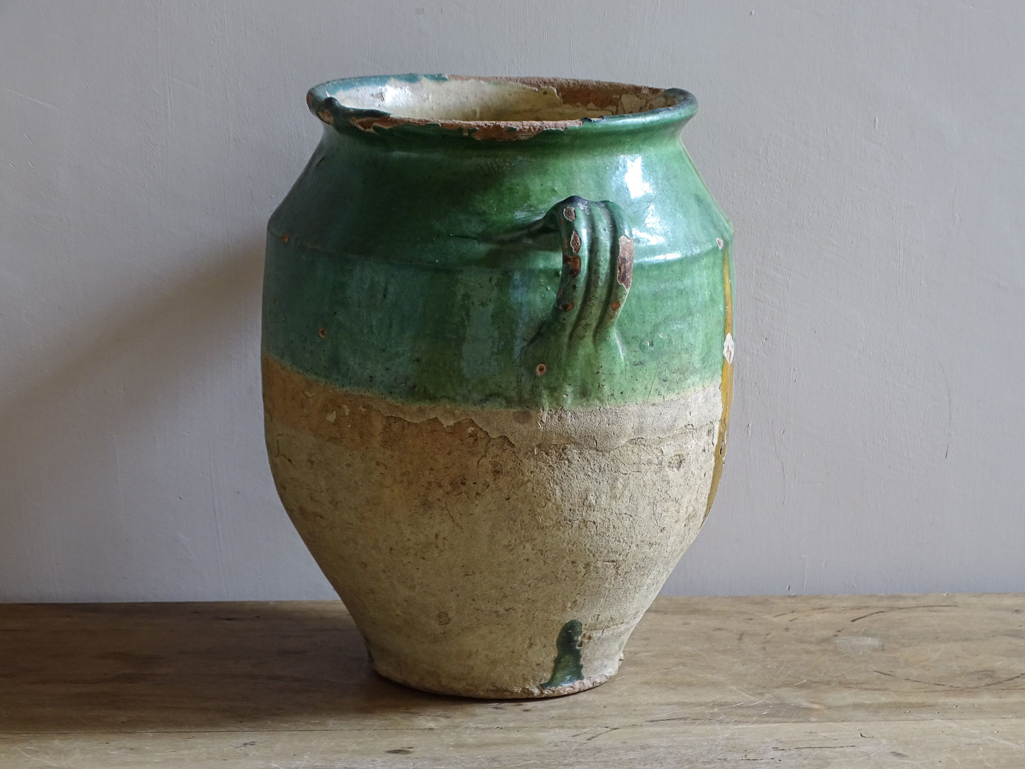 Antique French confit pot with unusual turquoise-green and mustard-yellow glaze, twin handles and a heavily weathered earthenware surface.