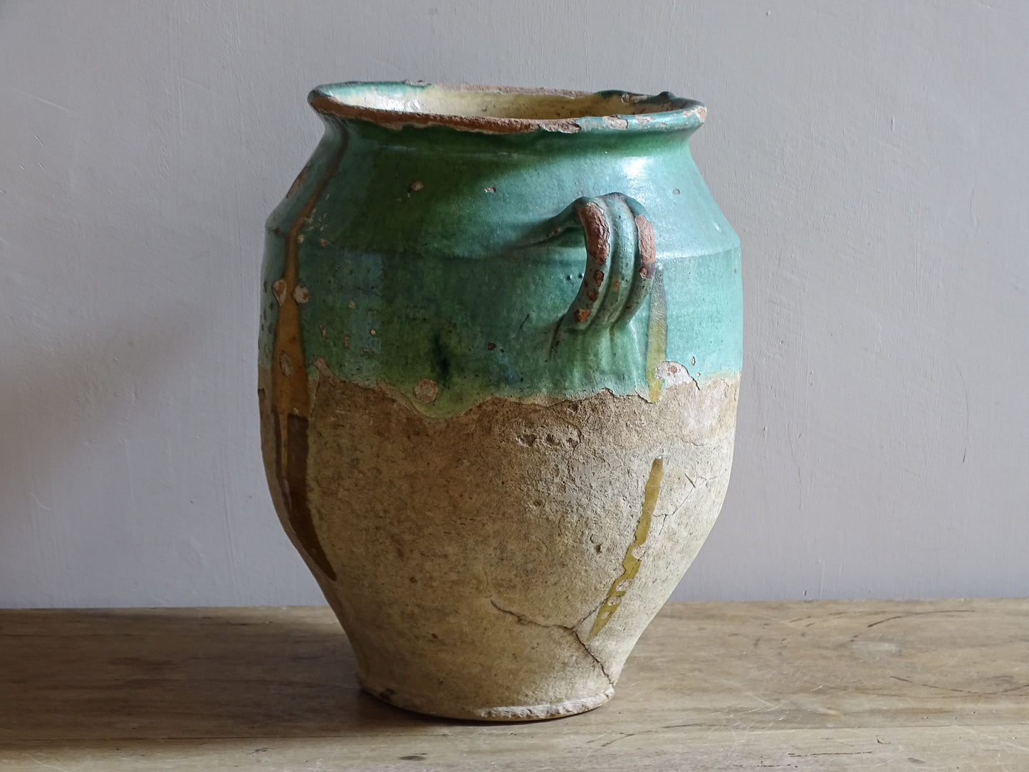 Antique French confit pot with unusual turquoise-green and mustard-yellow glaze, twin handles and a heavily weathered earthenware surface.