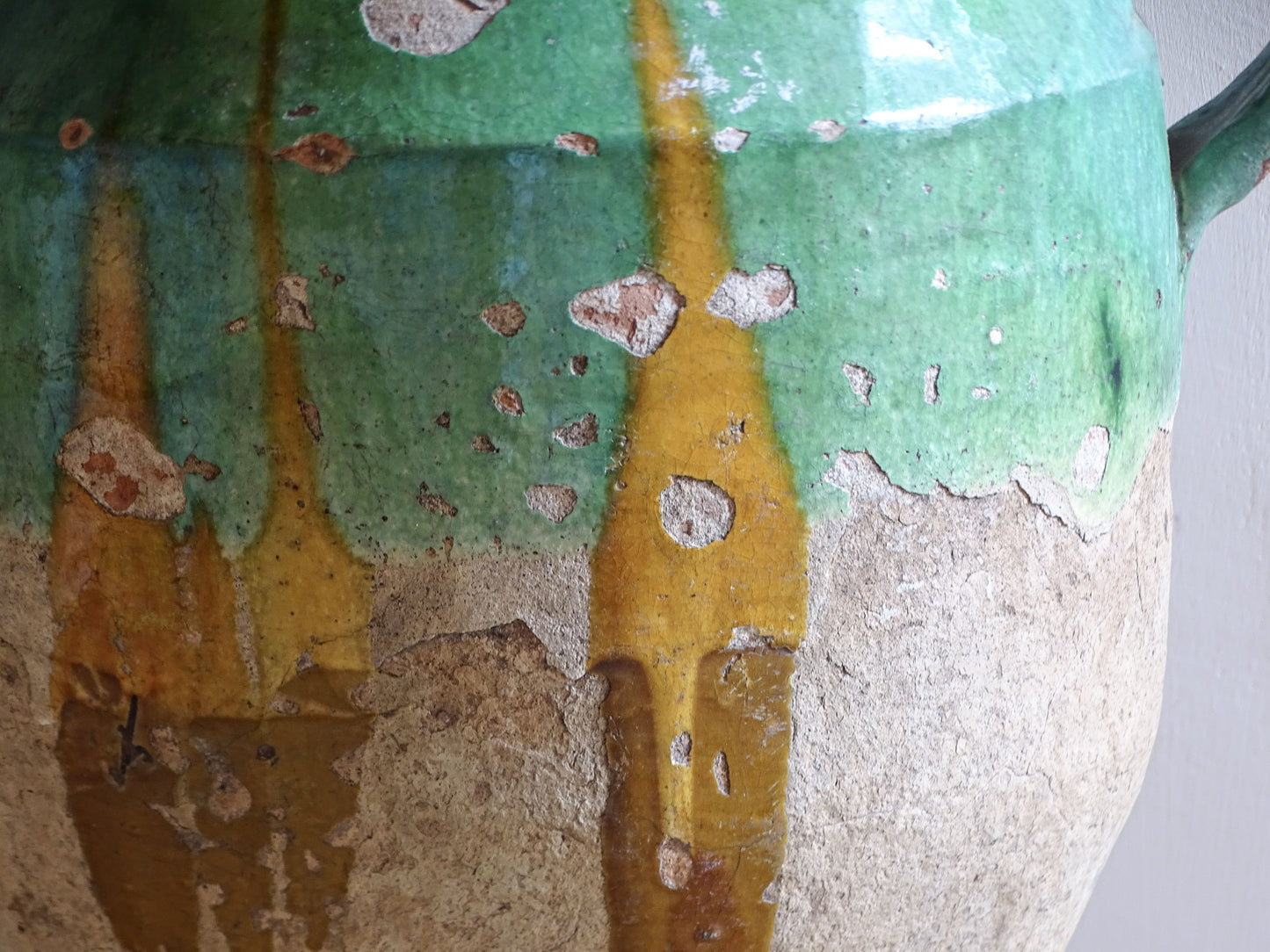 Antique French confit pot with unusual turquoise-green and mustard-yellow glaze, twin handles and a heavily weathered earthenware surface.