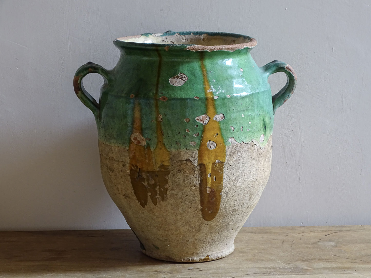 Antique French confit pot with unusual turquoise-green and mustard-yellow glaze, twin handles and a heavily weathered earthenware surface.