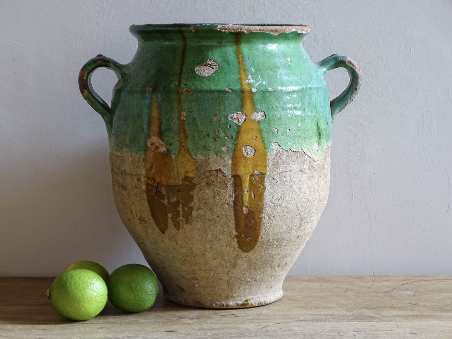 Antique French confit pot with unusual turquoise-green and mustard-yellow glaze, twin handles and a heavily weathered earthenware surface.