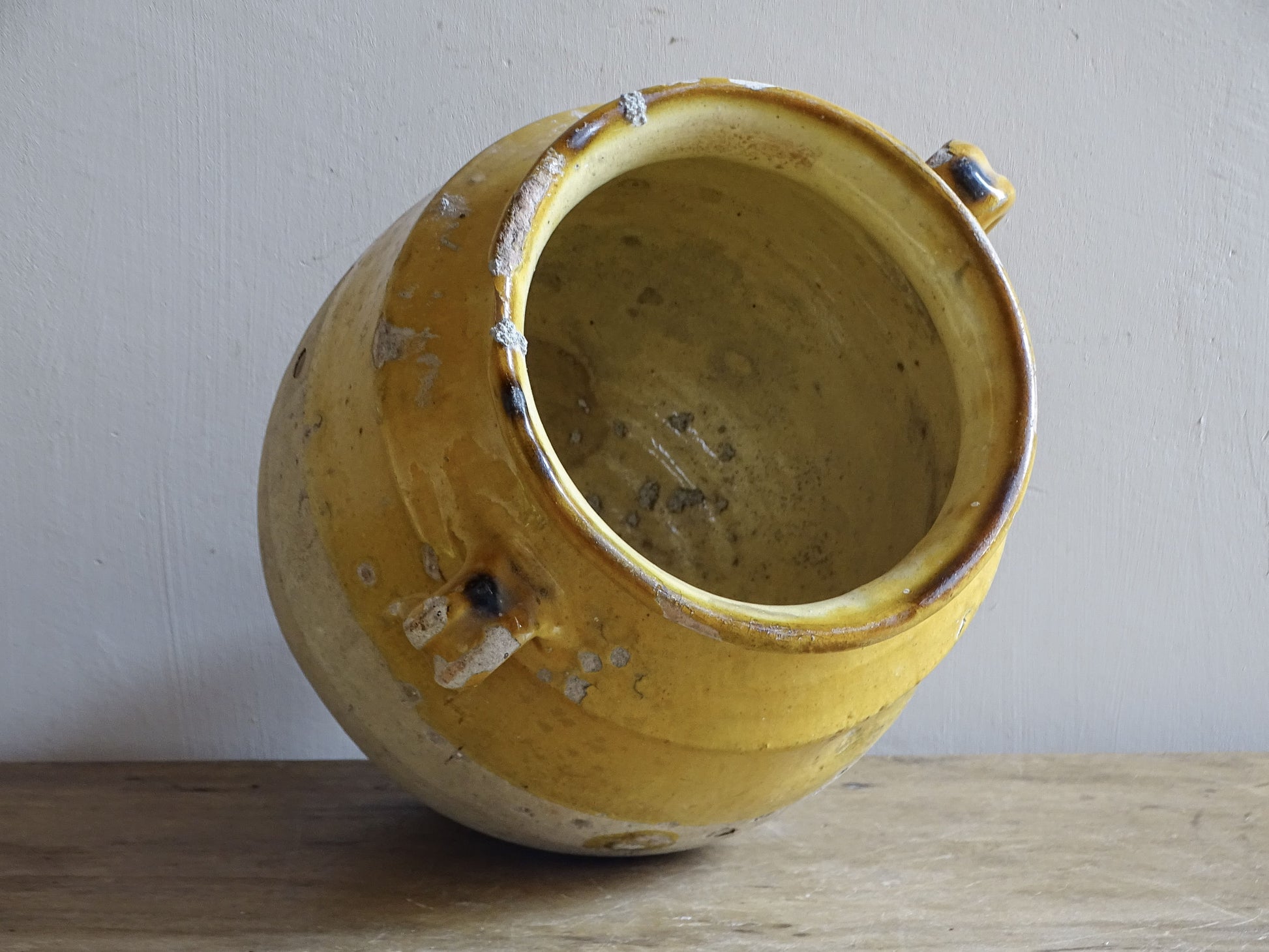 An antique French confit jar with yellow glaze and two looped handles.