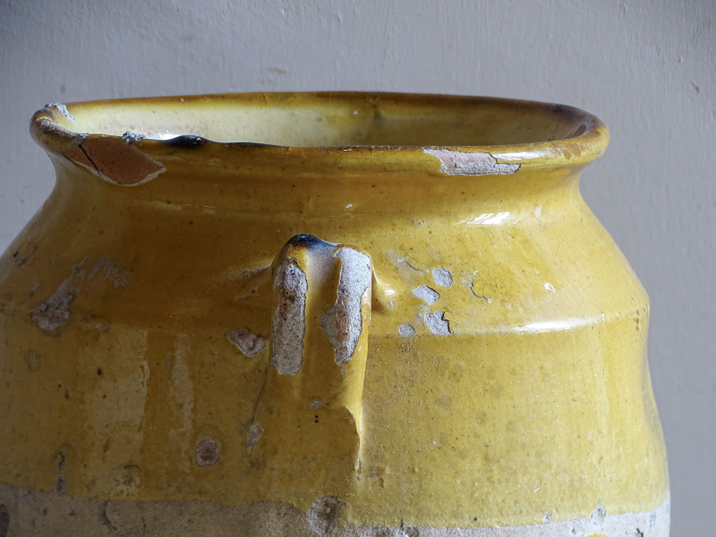 An antique French confit pot with yellow glaze and two looped handles.