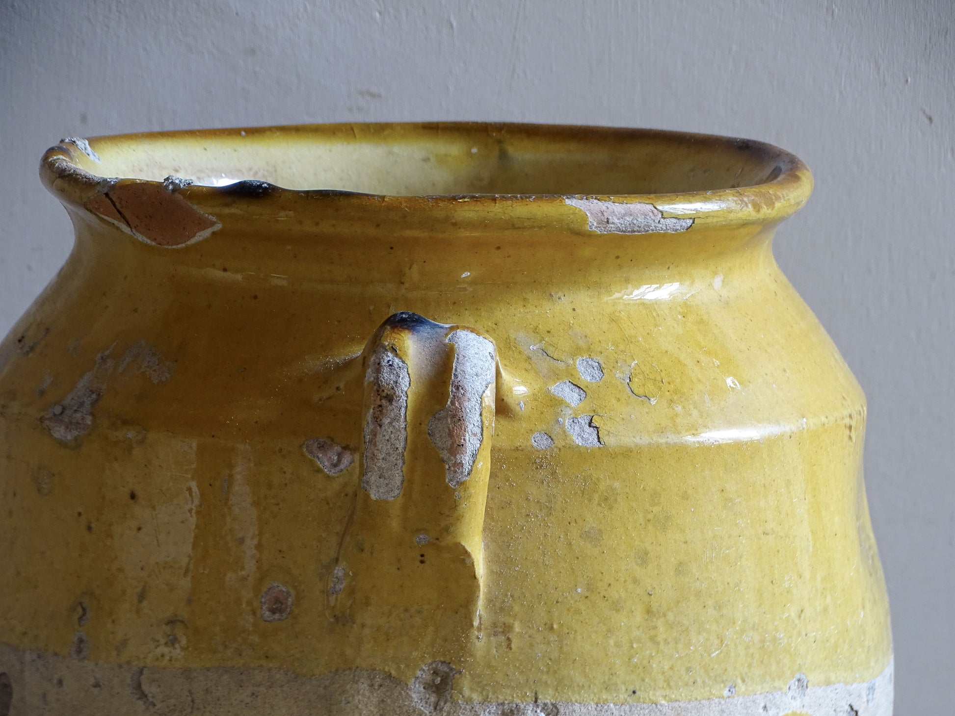 An antique French confit pot with yellow glaze and two looped handles.
