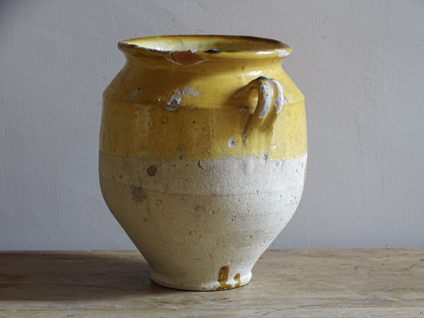 An antique French confit pot with yellow glaze and two looped handles.