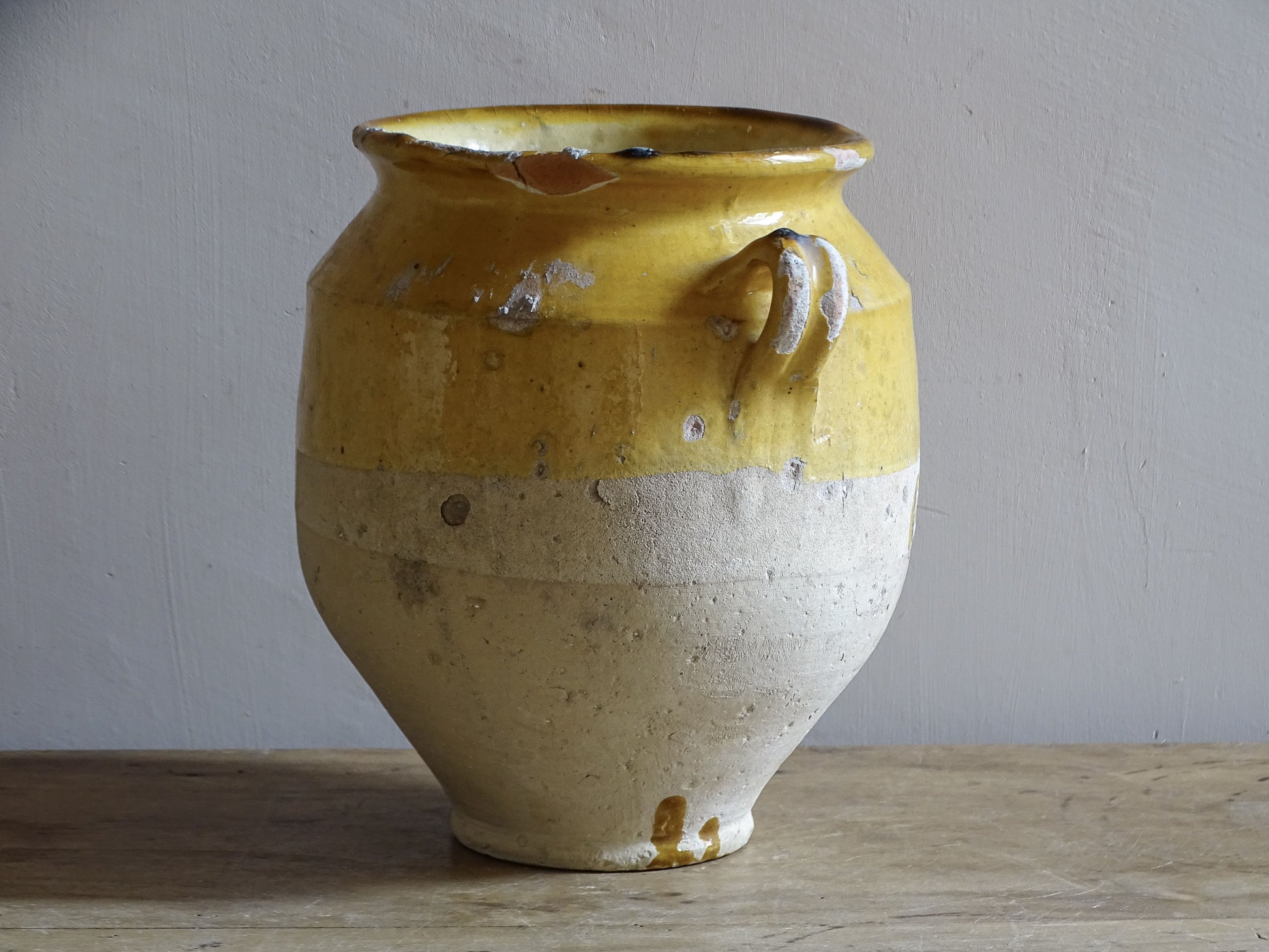 An antique French confit pot with yellow glaze and two looped handles.