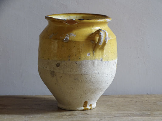An antique French confit pot with yellow glaze and two looped handles.