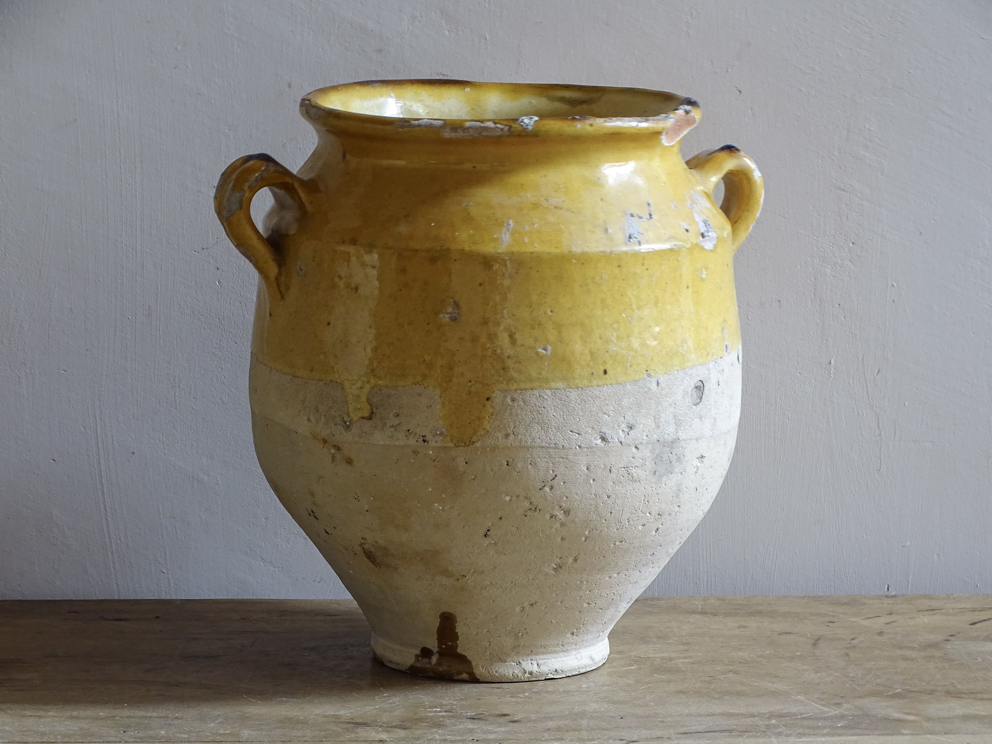 An antique French confit pot with yellow glaze and two looped handles.