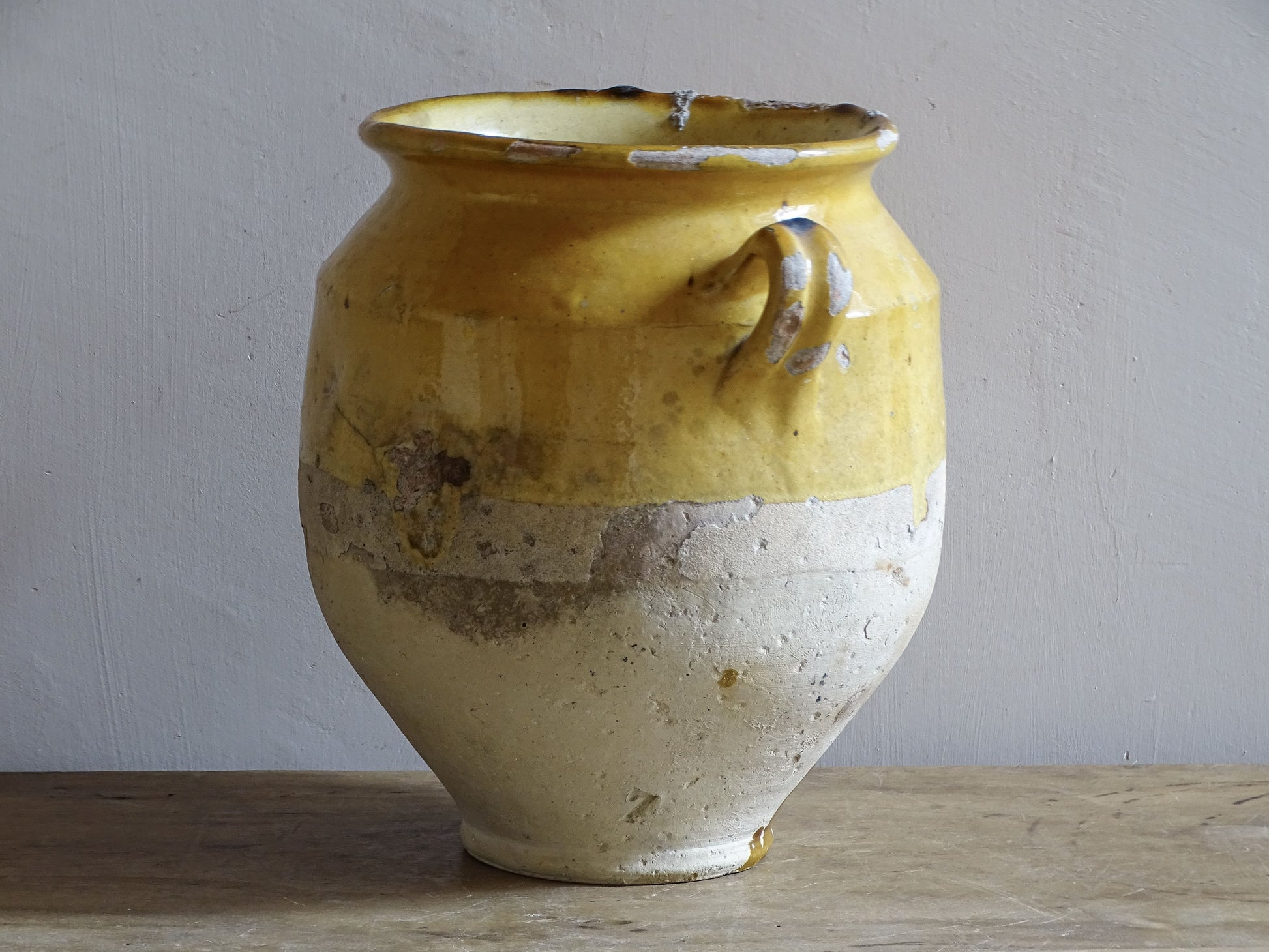 An antique French confit pot with yellow glaze and two looped handles.