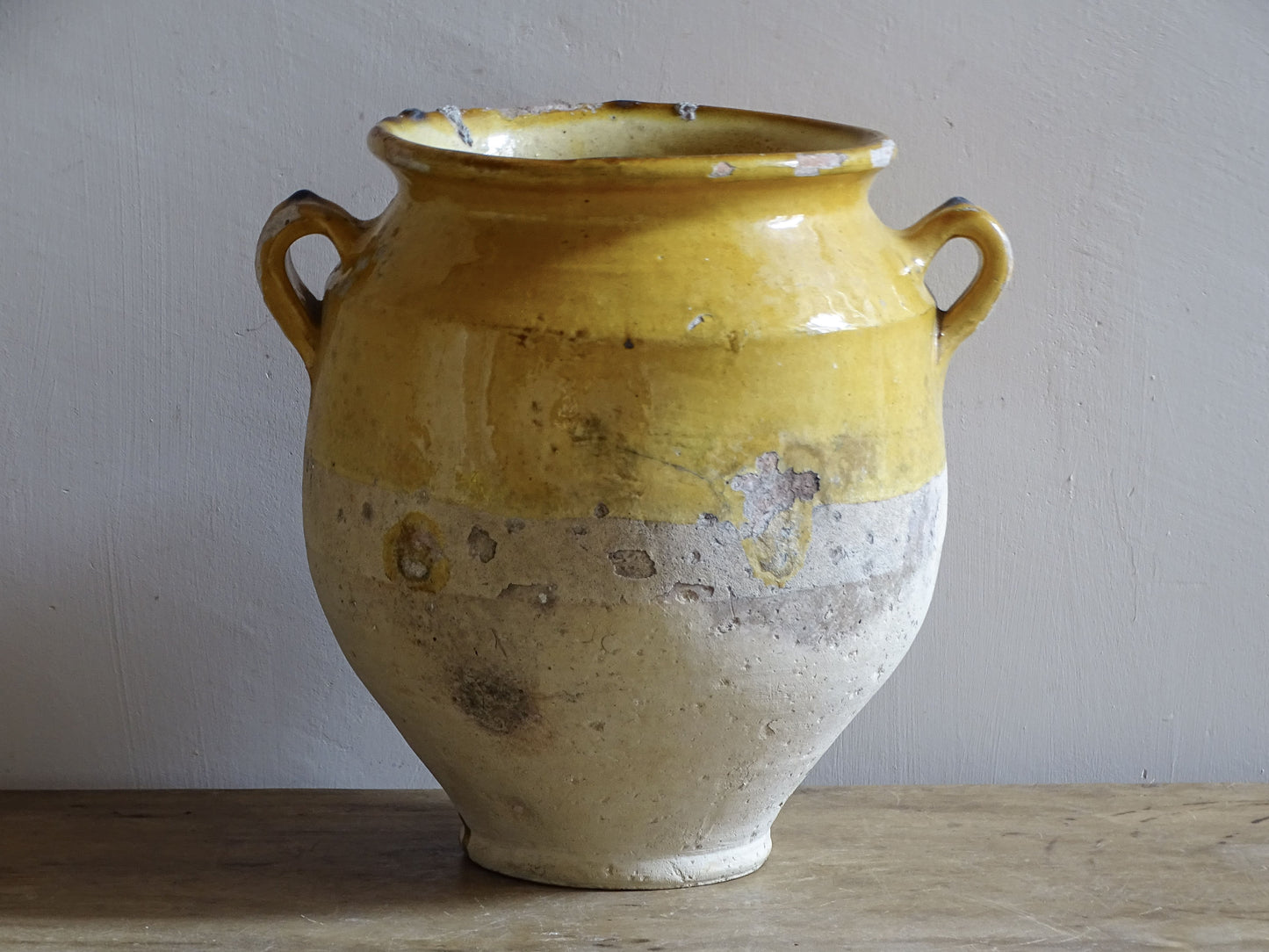 An antique French confit pot with yellow glaze and two looped handles.